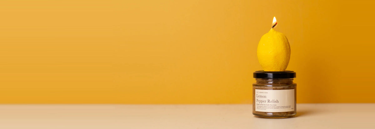 Women's Work lemon candle sitting on a jar of Lemon Pepper Relish against a warm yellow backdrop