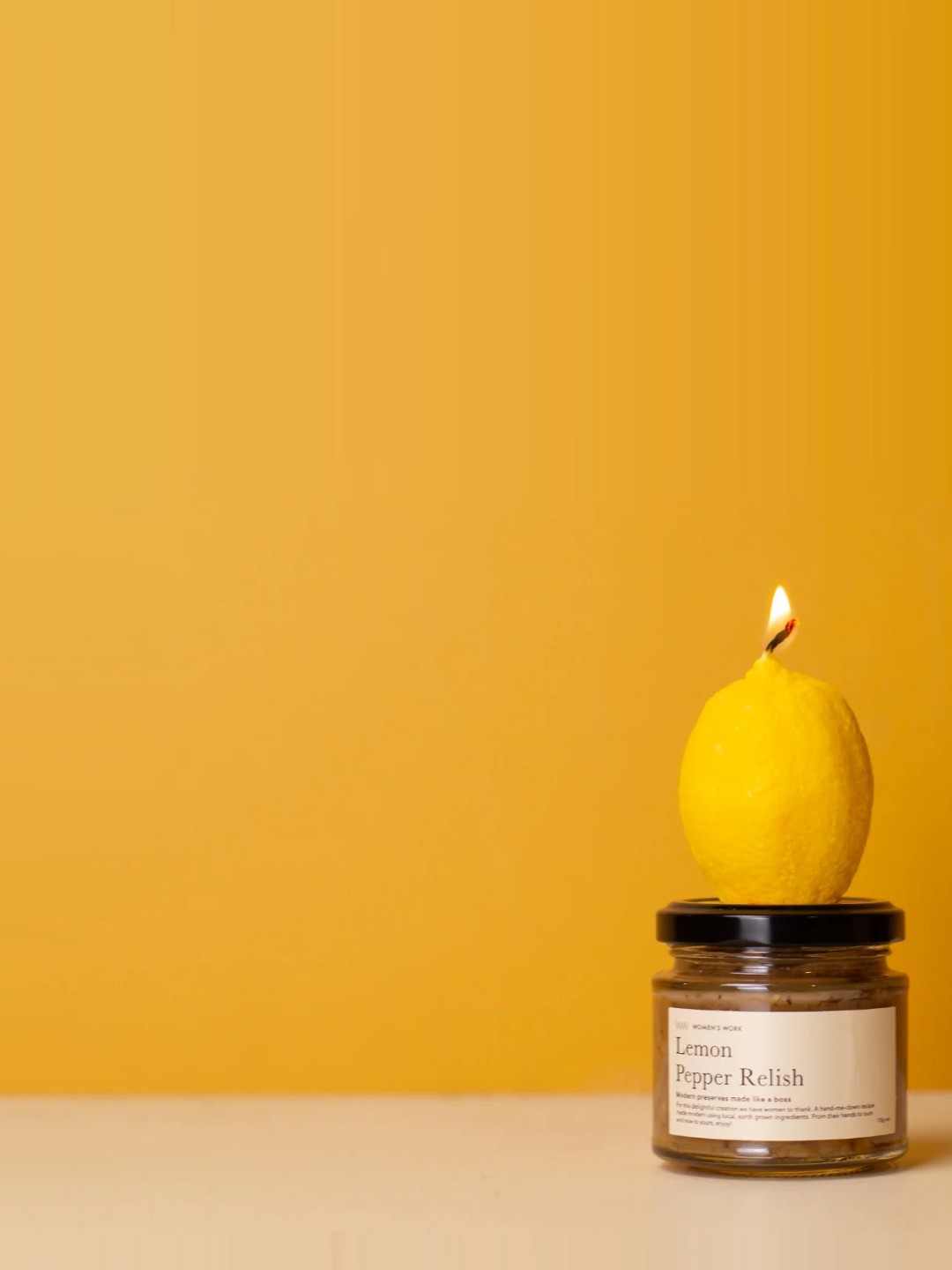 Women's Work lemon candle sitting on a jar of Lemon Pepper Relish against a warm yellow backdrop